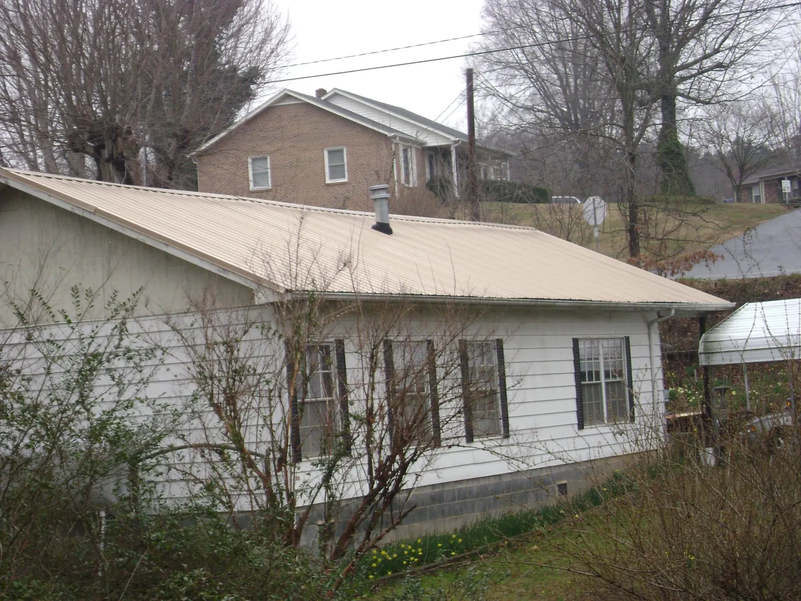 Tan metal roof on a white sided house set into a hillside — Commercial Roofing by Roofing Brothers in Ocean Beach