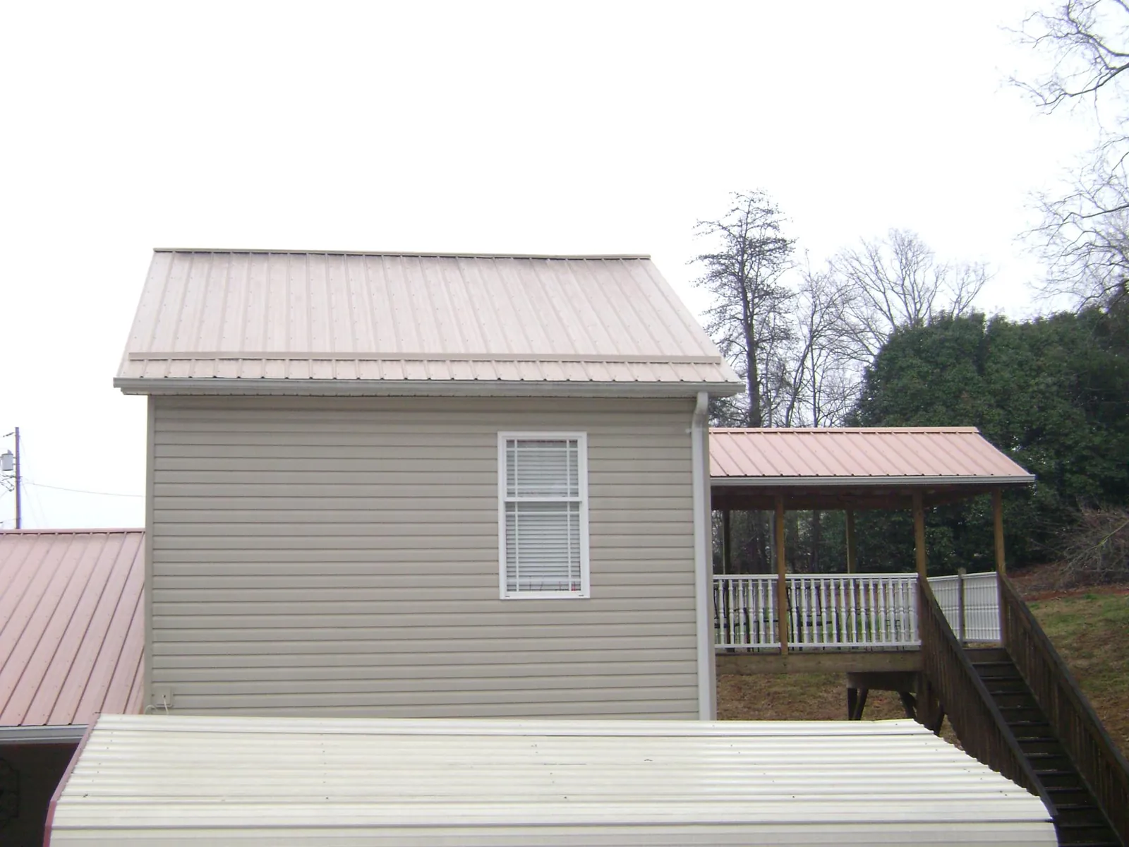 Tan metal roofs on a two story addition and attached porch, from a Roof Replacement job in Ocean Beach